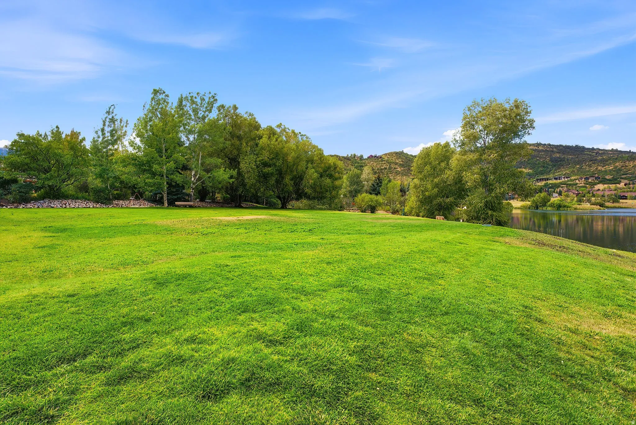 Expansive grassy lawn with established trees and a tranquil body of water