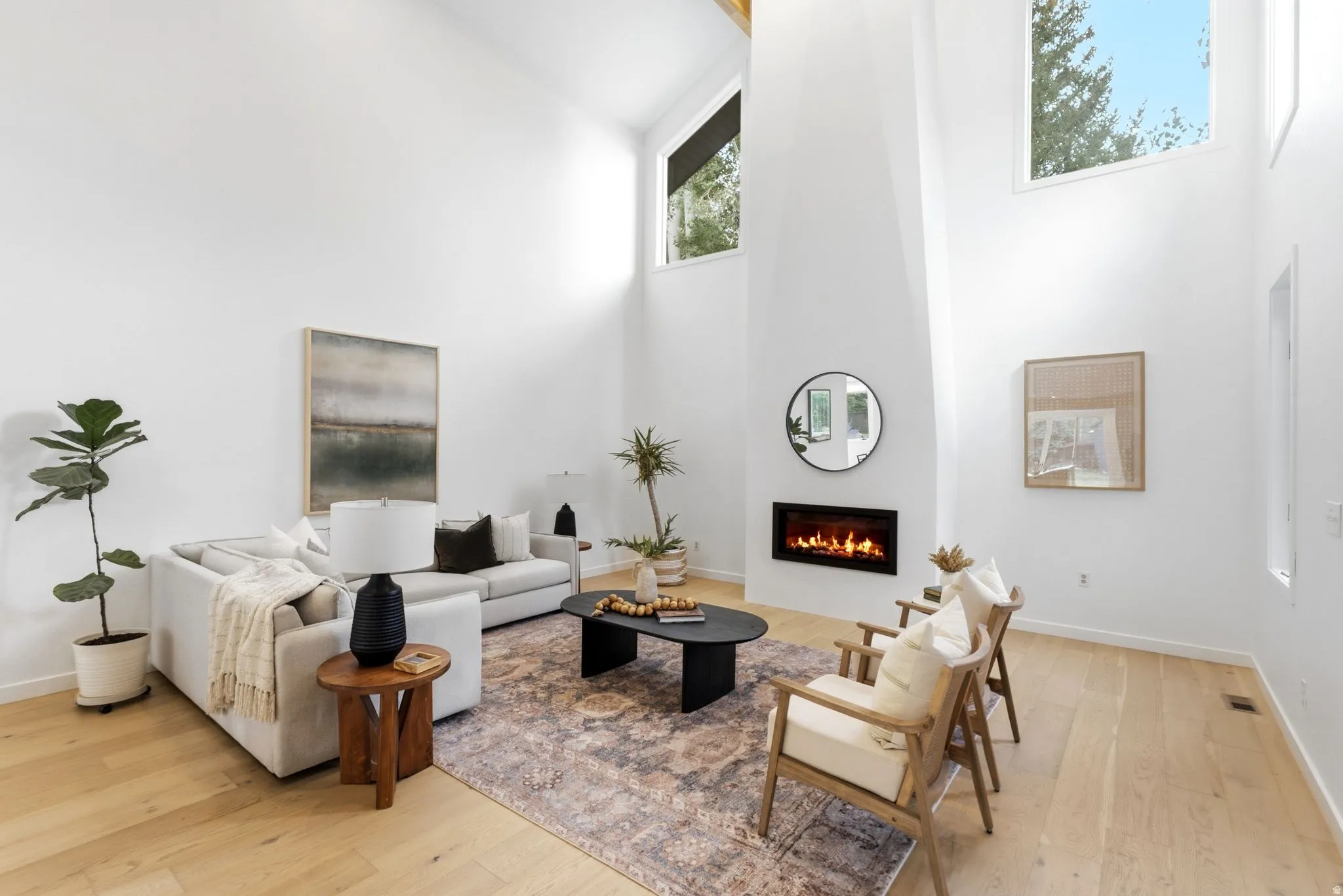 Vaulted ceilings with clerestory windows, wood-finish flooring, a wall-mounted fireplace, and light-toned walls