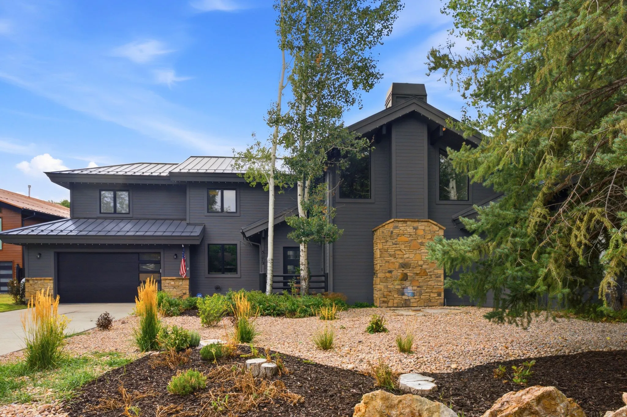 Modern exterior featuring dark siding, stone accents, multiple large windows, a metal roof, and an attached garage