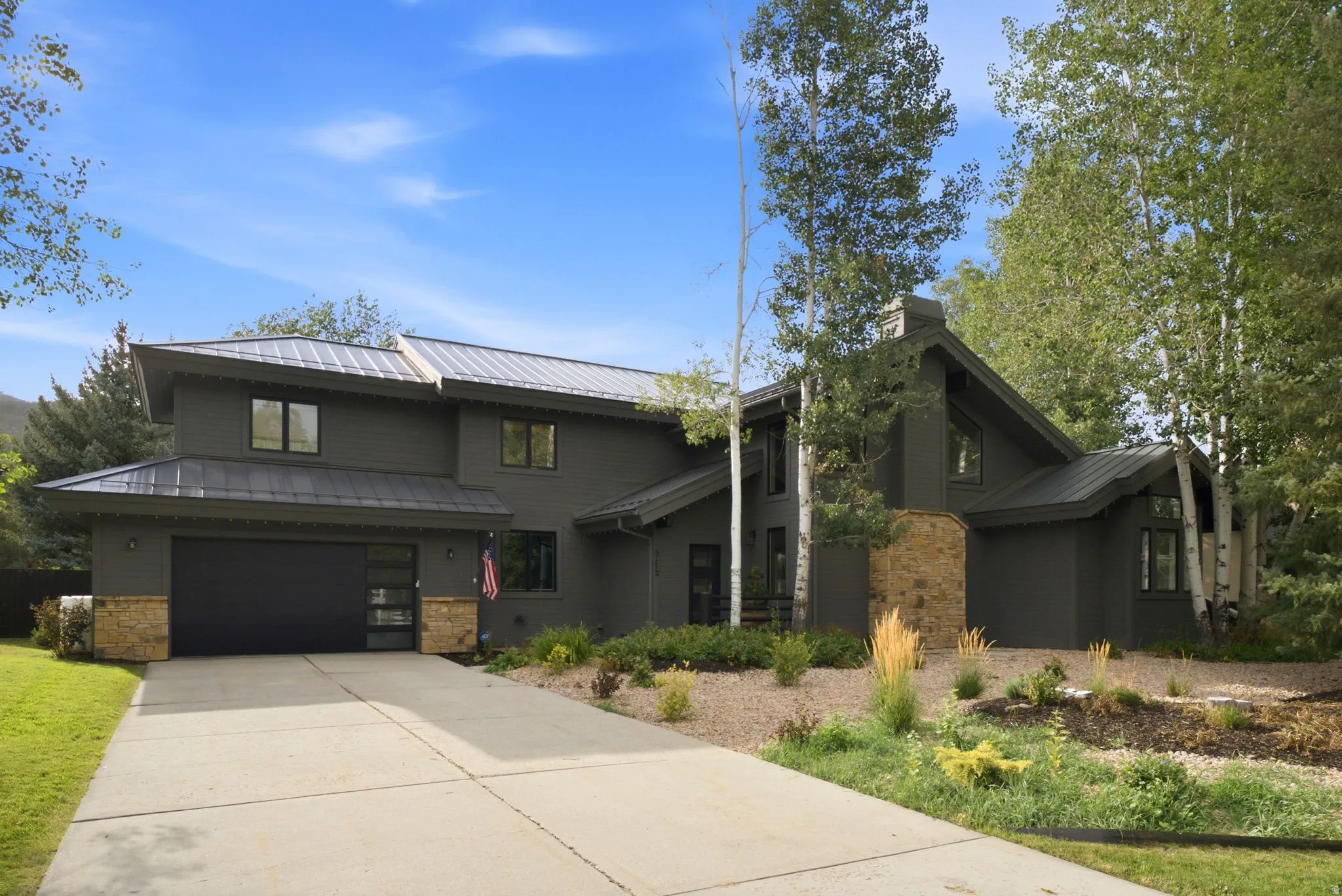 Contemporary exterior with a dark siding finish, stone accents, a metal roof, an attached garage, and a concrete driveway