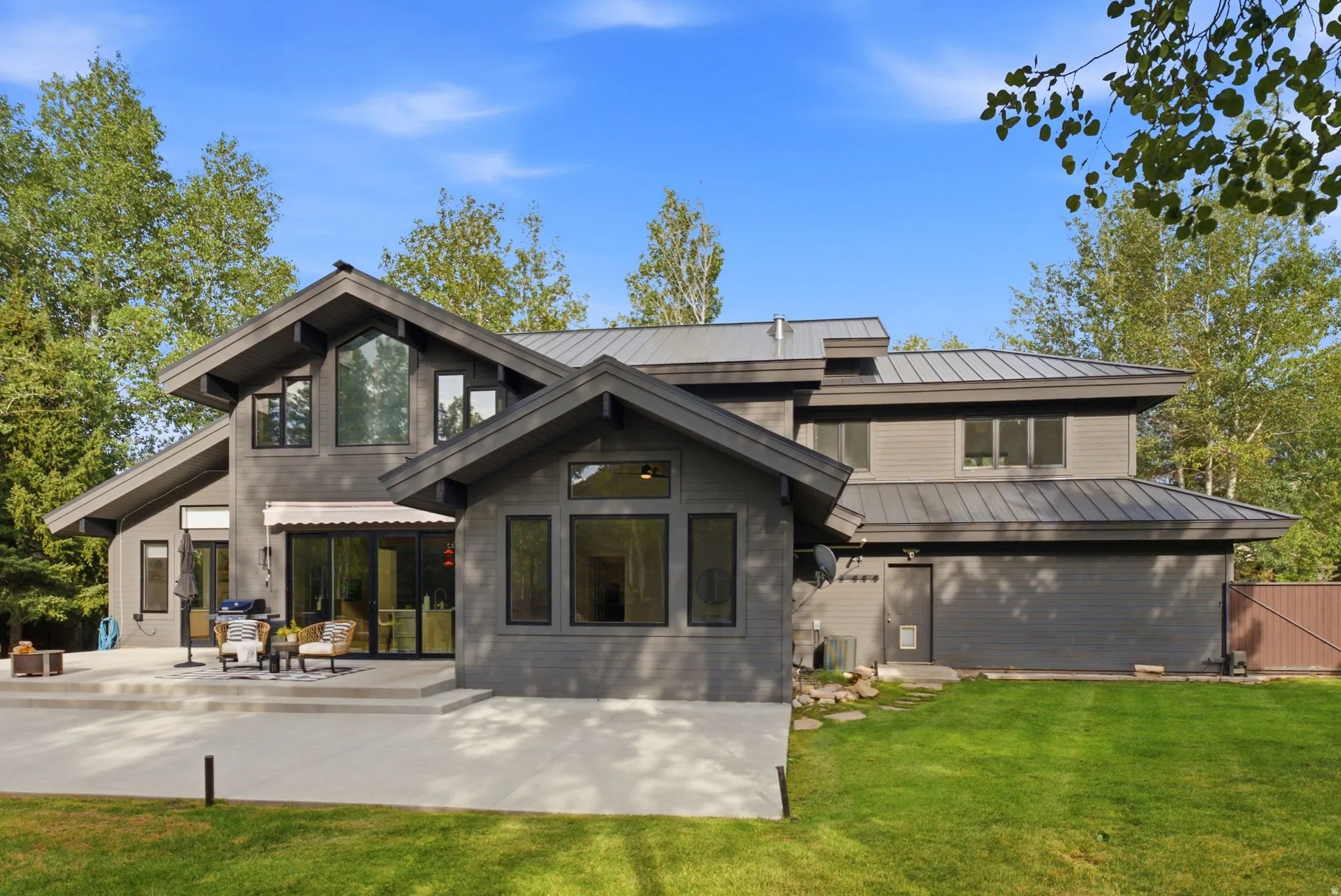 Contemporary exterior with multiple rooflines, a metal roof, an expansive concrete patio, and mature trees