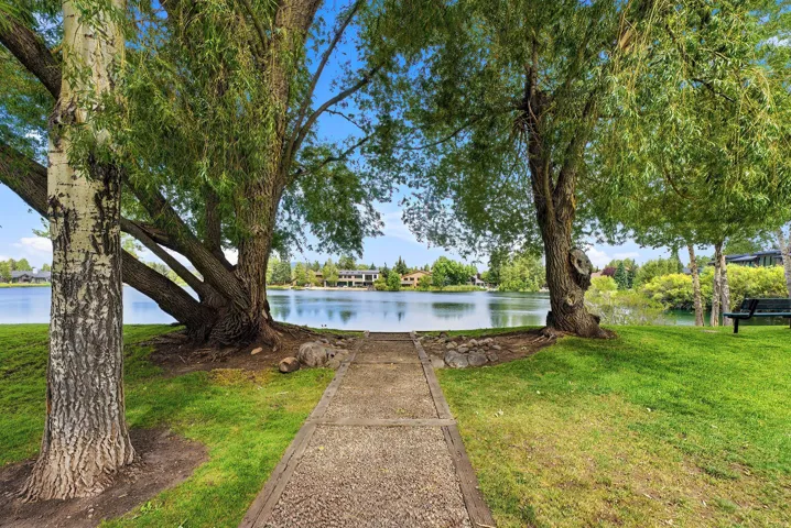 Manicured lawn with mature trees and a paved pathway leading to the water's edge