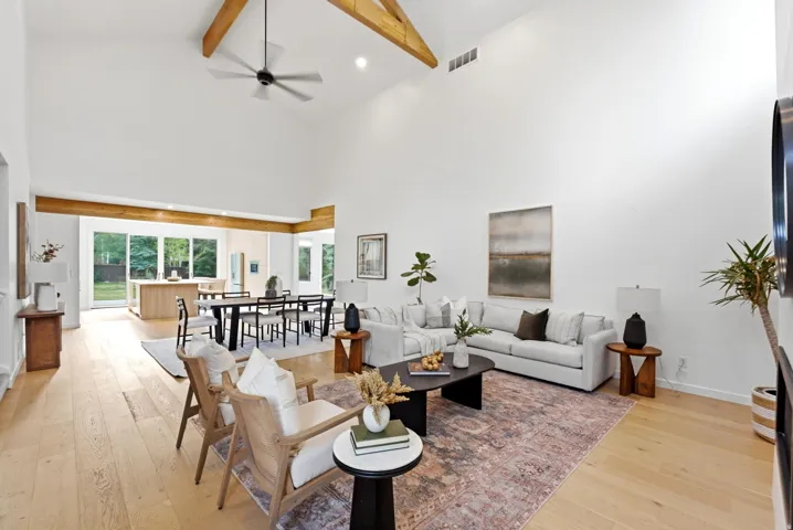 Vaulted ceilings with exposed wood beams, light wood-finish flooring, a contemporary ceiling fan, and sliding glass doors