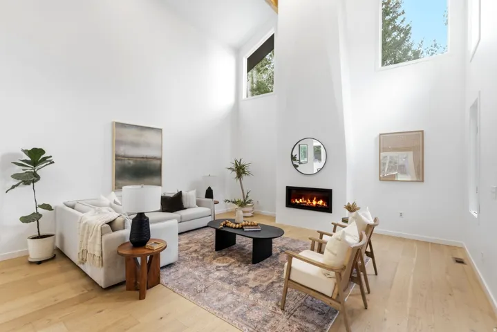 Vaulted ceilings with clerestory windows, wood-finish flooring, a wall-mounted fireplace, and light-toned walls