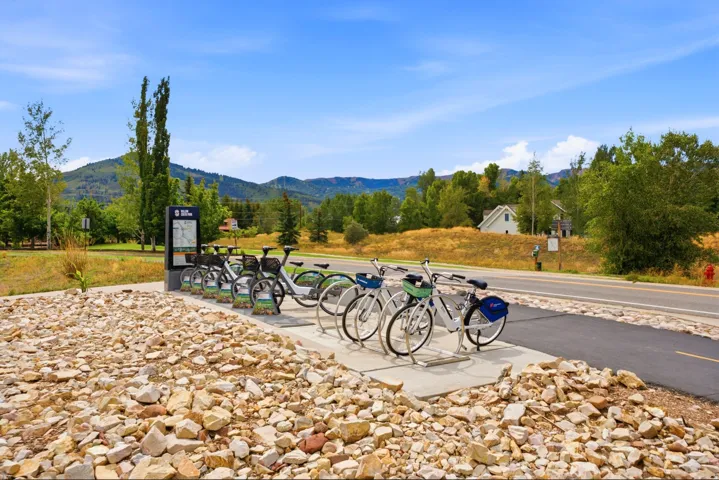 Paved pathway, bike share station, natural rock landscaping, distant mountain scenery, and mature trees