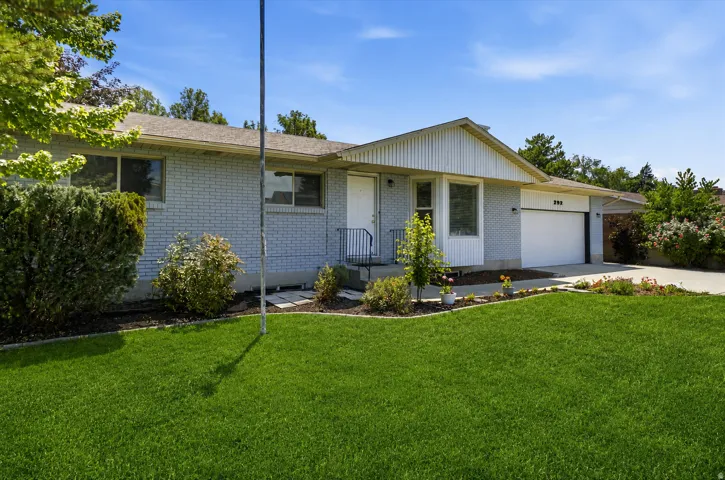 Brick exterior with a peaked roofline, an attached garage, a concrete driveway, and front landscaping