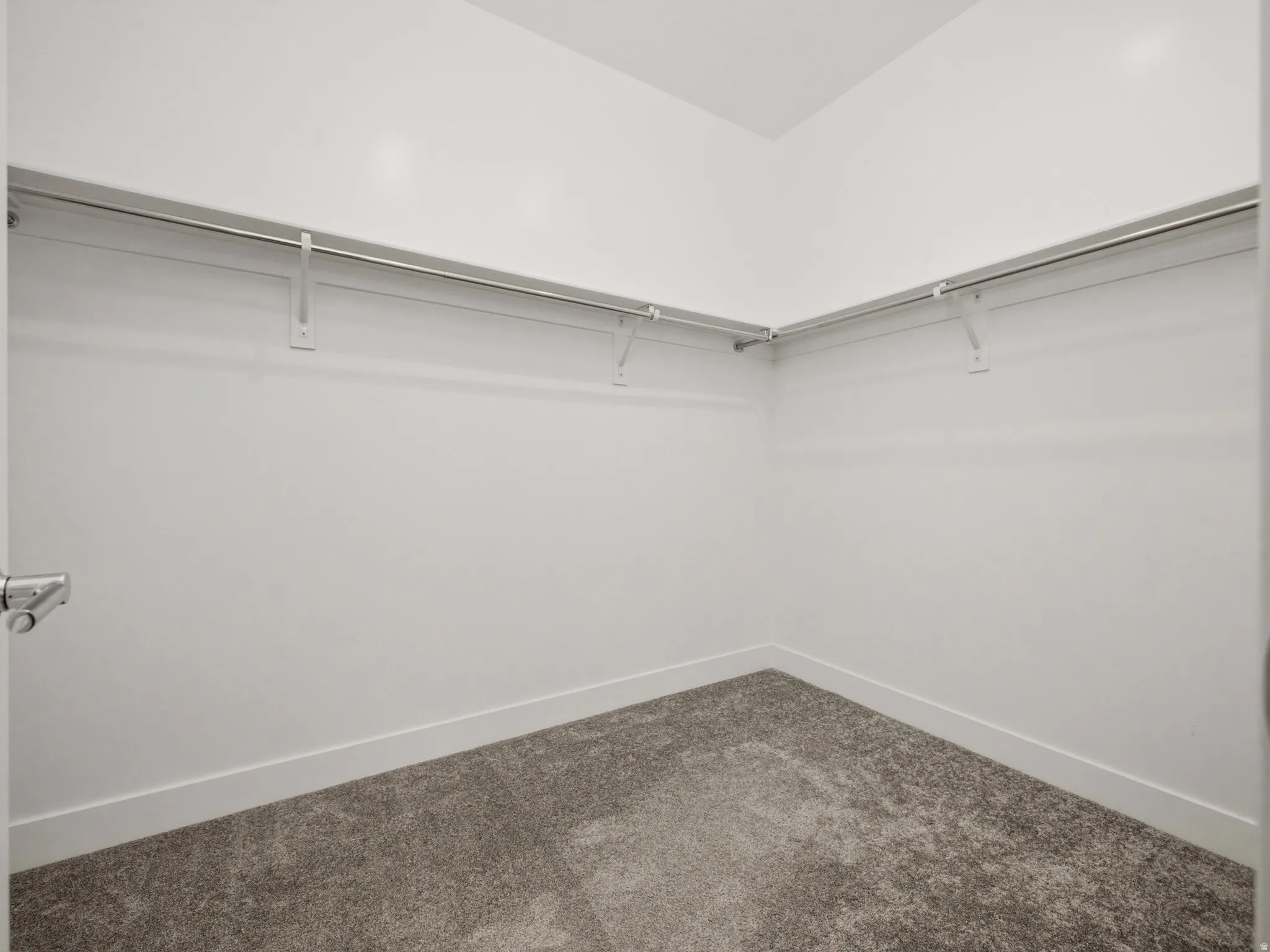 Walk-in closet featuring white walls, durable gray carpeting, and ample hanging rods