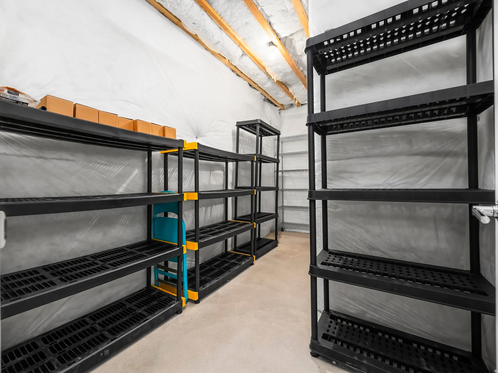 Utility room featuring exposed ceiling joists with insulation, concrete flooring, and multiple shelving units