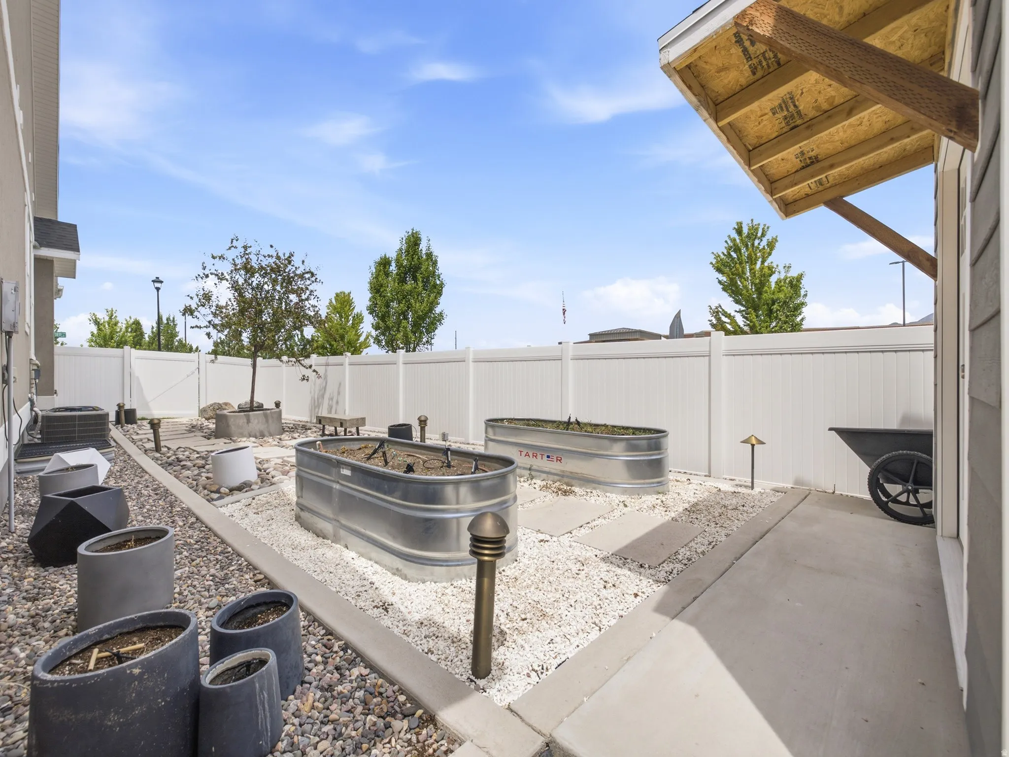Private backyard space featuring a white vinyl fence, two galvanized planters, and a concrete patio section