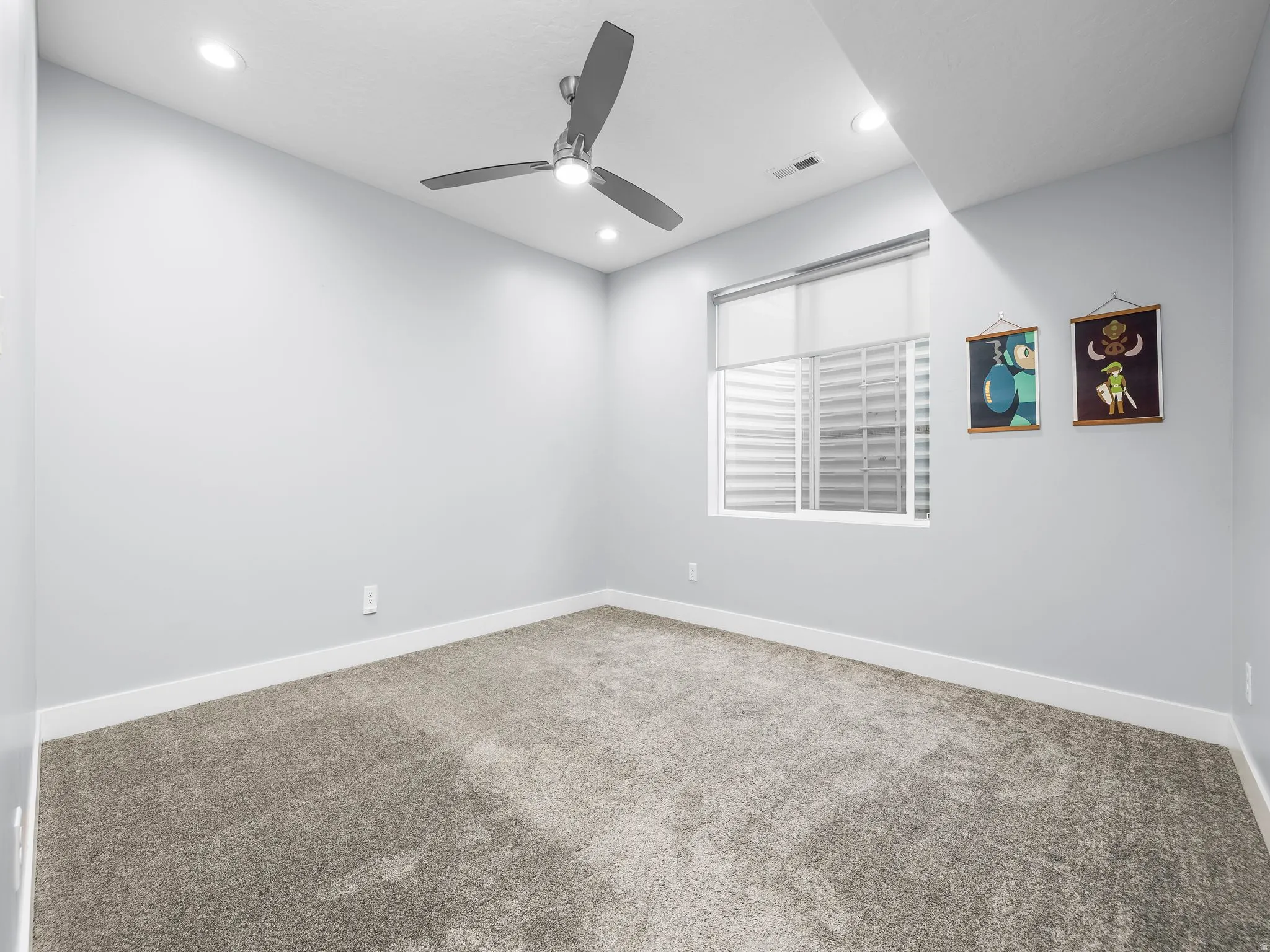 Neutral-toned carpeted room featuring a ceiling fan with integrated lighting, recessed ceiling lights, a window with a roller shade, and white baseboards