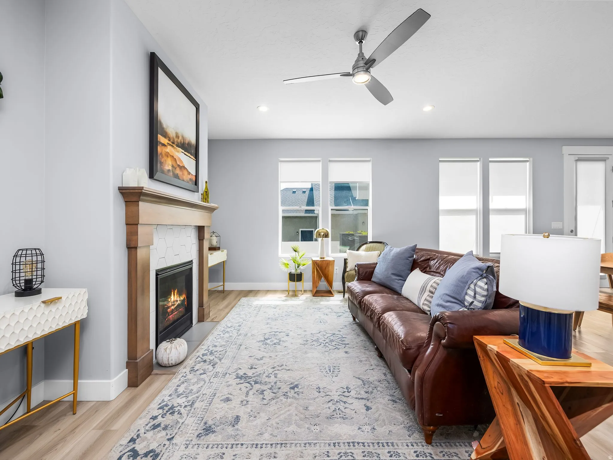 Living area featuring wood-finish flooring, a contemporary fireplace with a wood mantle and hexagonal tile surround, multiple windows, recessed lighting, and a ceiling fan