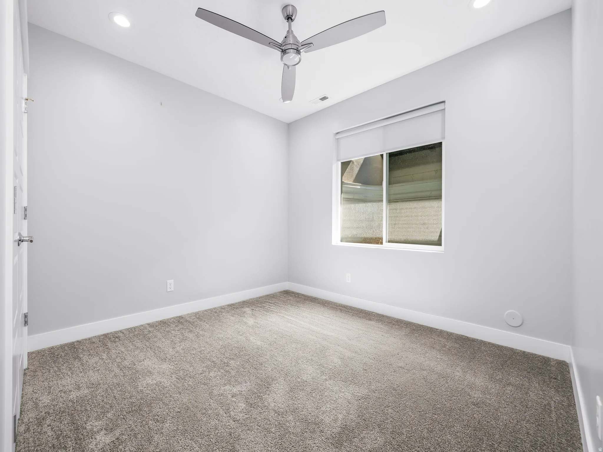 Room featuring recessed lighting, a modern ceiling fan, a window with roller shade, neutral wall tones, and gray carpet flooring