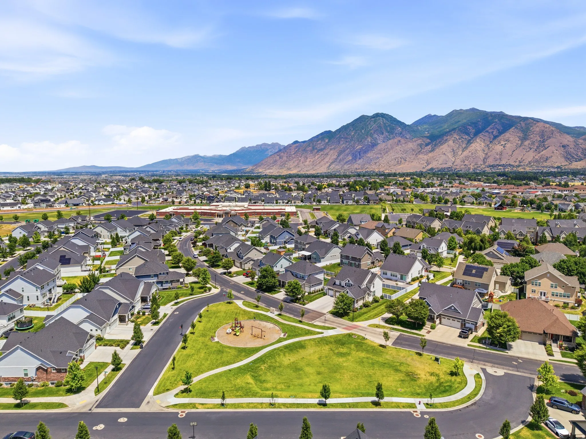 Expansive residential development featuring a community park, paved streets, and a mountainous backdrop