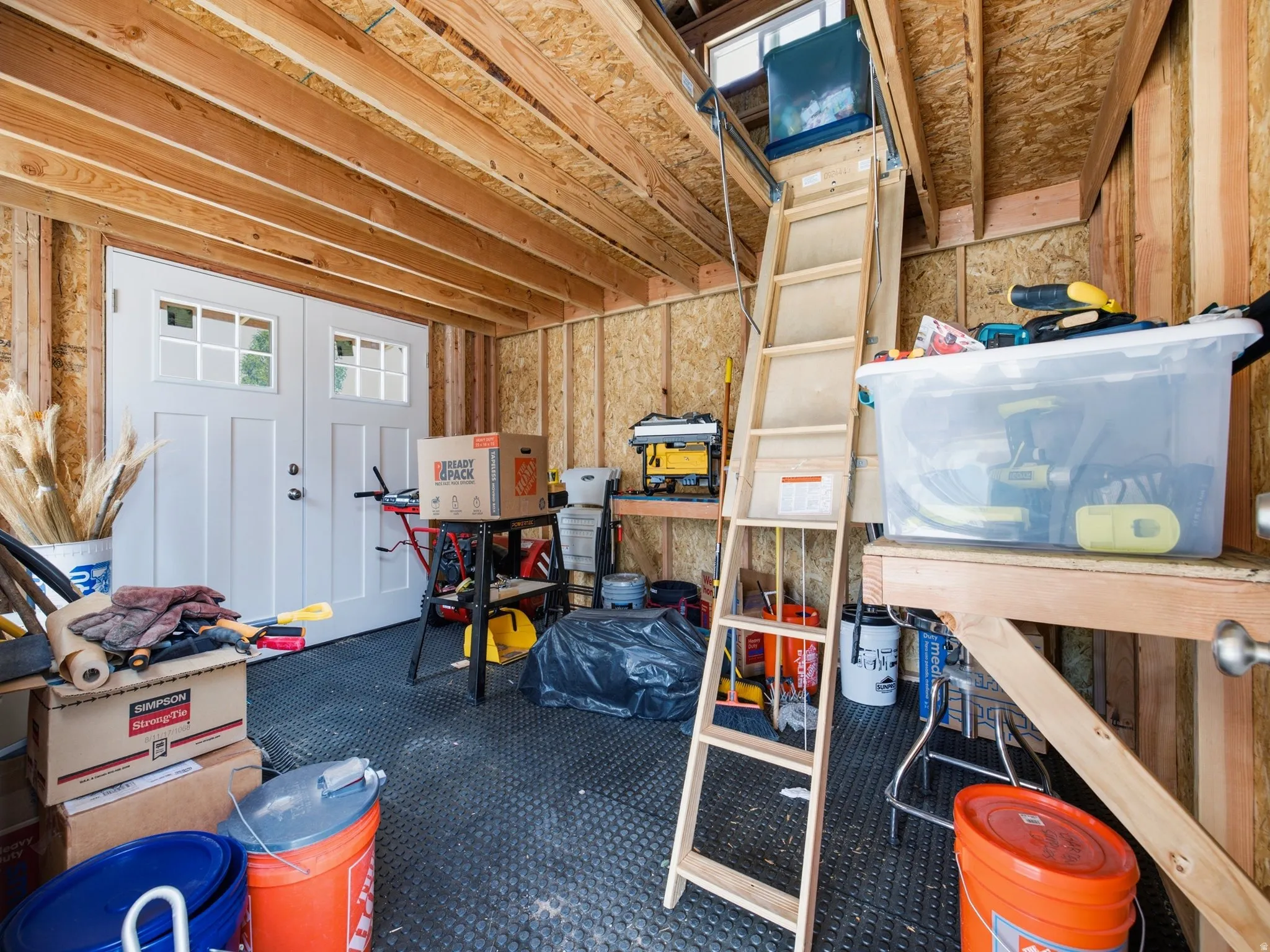 Utility shed interior featuring exposed wood beam ceiling, plywood walls, and rubberized flooring