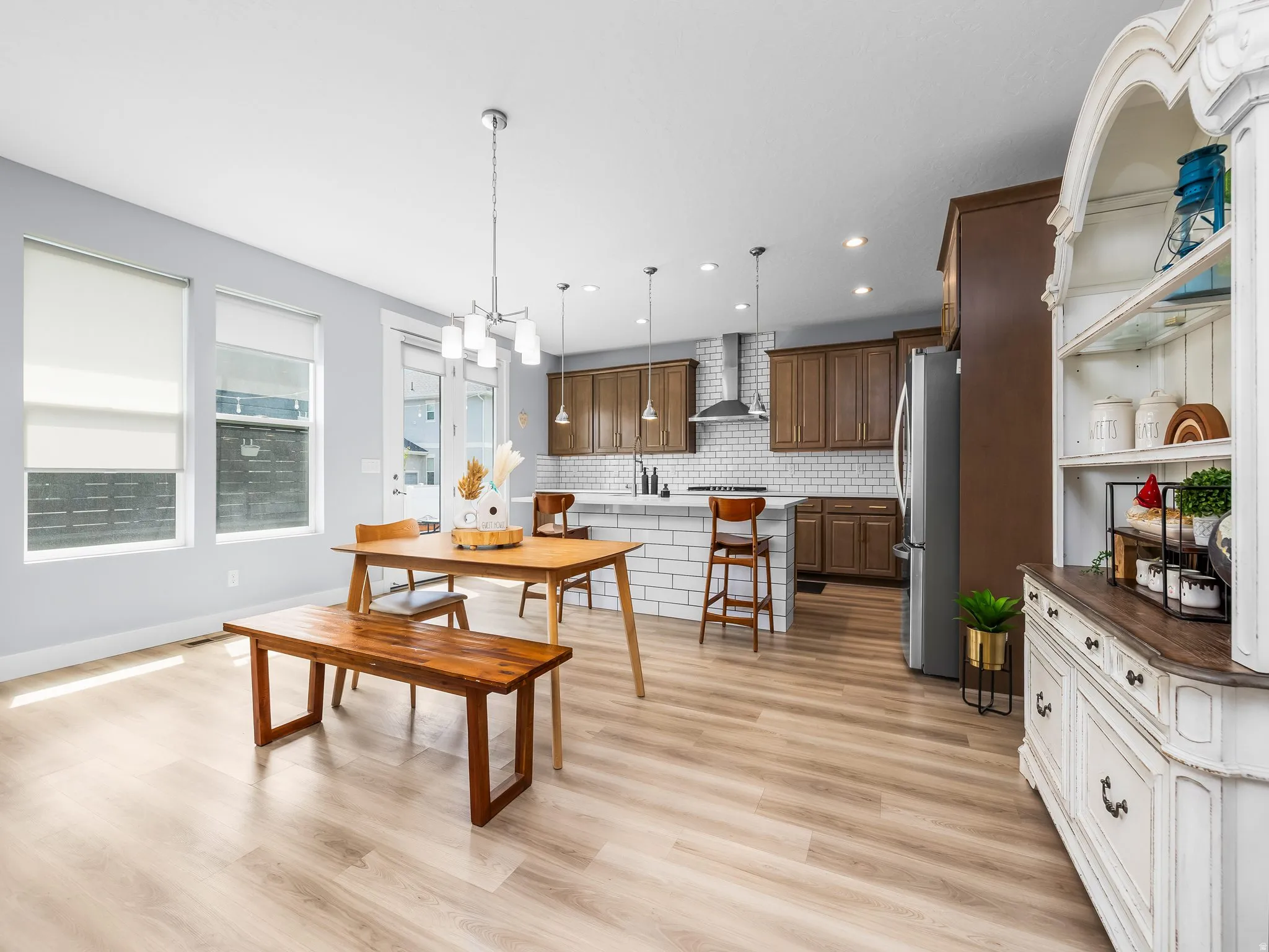 Open-concept living space featuring wood-finish flooring, a contemporary kitchen with a subway tile backsplash, stainless steel appliances, and dark wood cabinetry