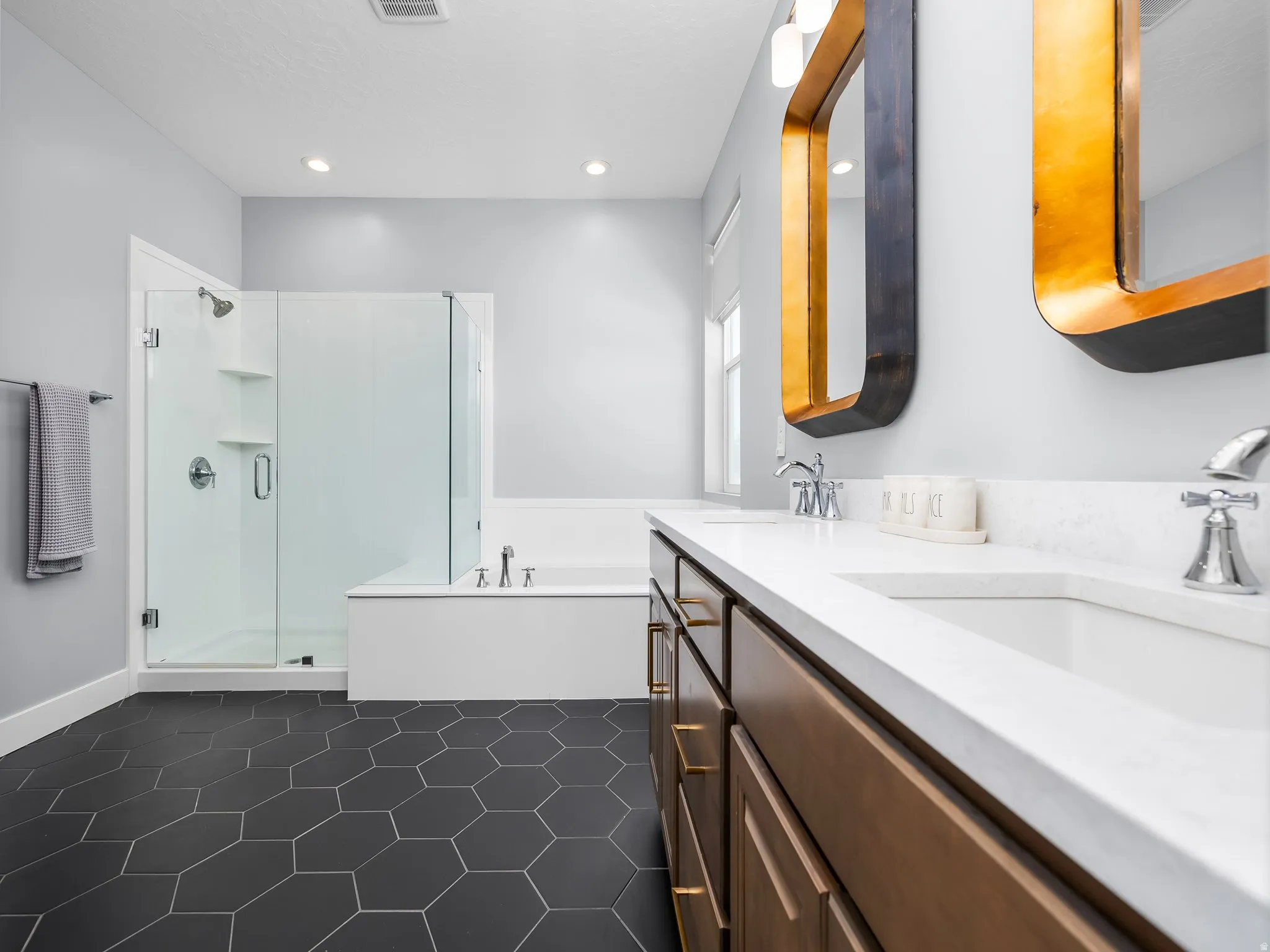 Dual vanity with white countertops, wood-finish cabinetry, and gold-framed mirrors