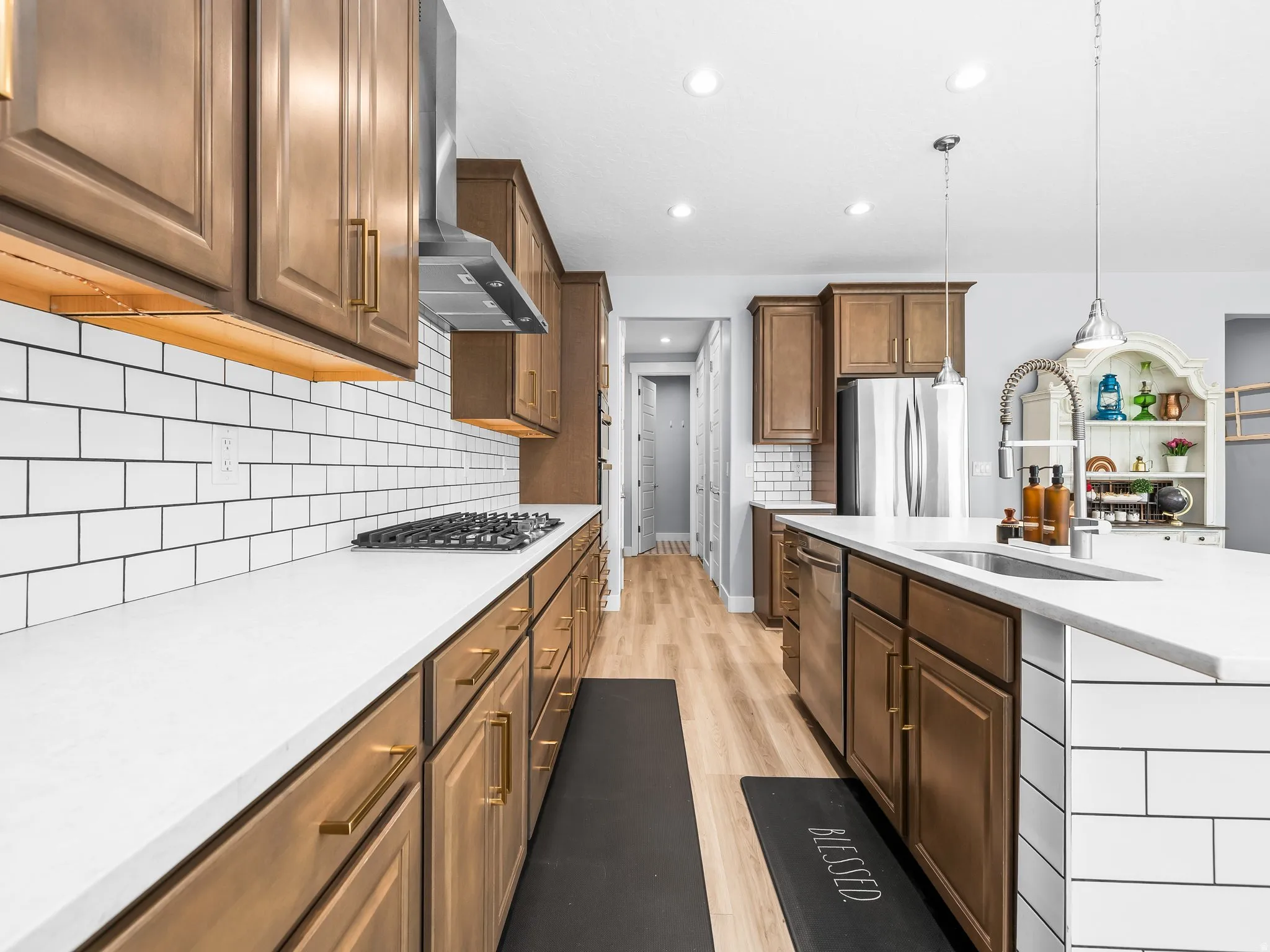 Spacious kitchen featuring warm wood-finish cabinetry with golden hardware, white countertops, and a subway tile backsplash