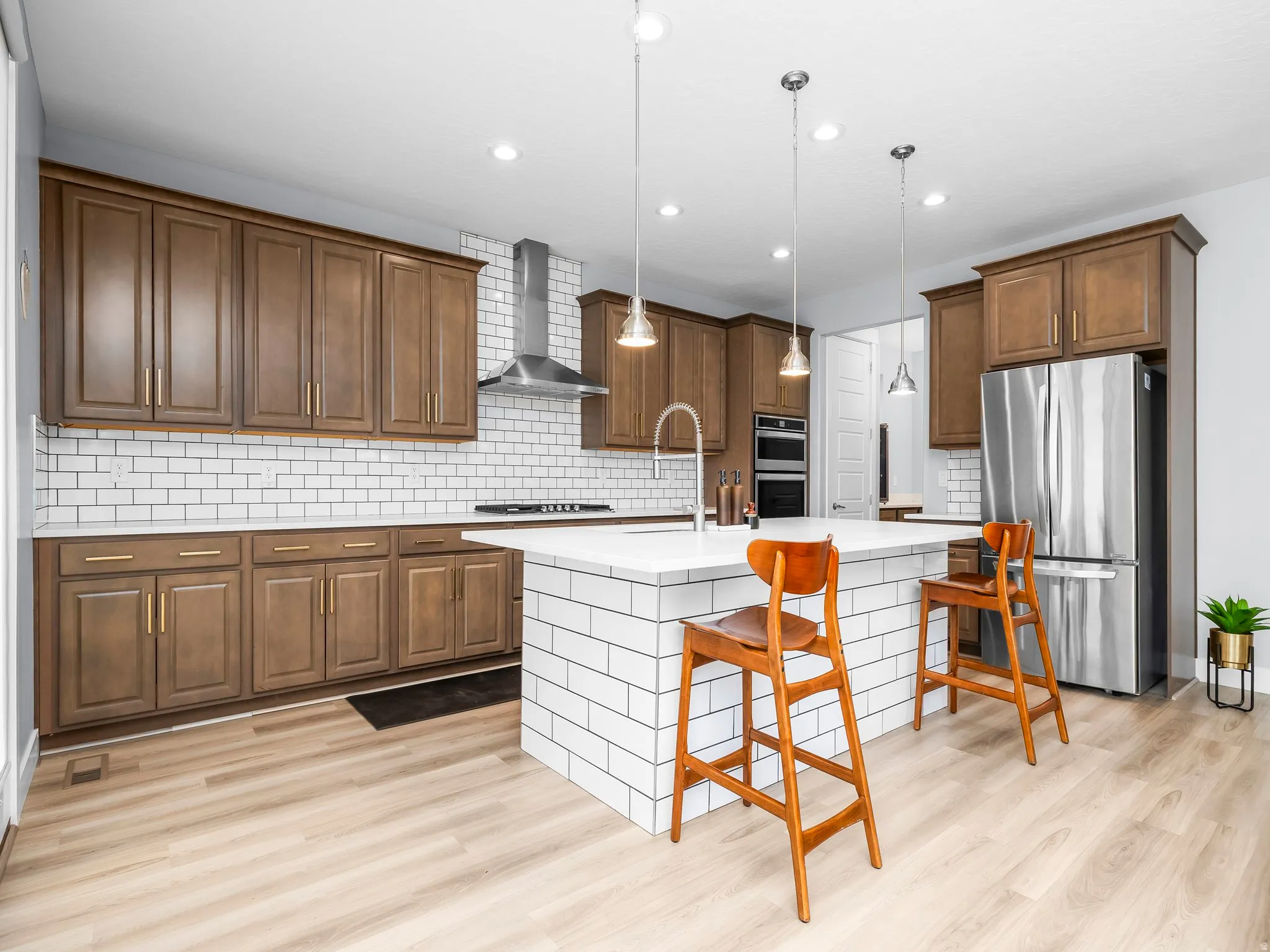 Modern kitchen featuring wood-finish cabinetry, stainless steel appliances, a subway tile backsplash, recessed lighting, and a kitchen island with pendant lighting