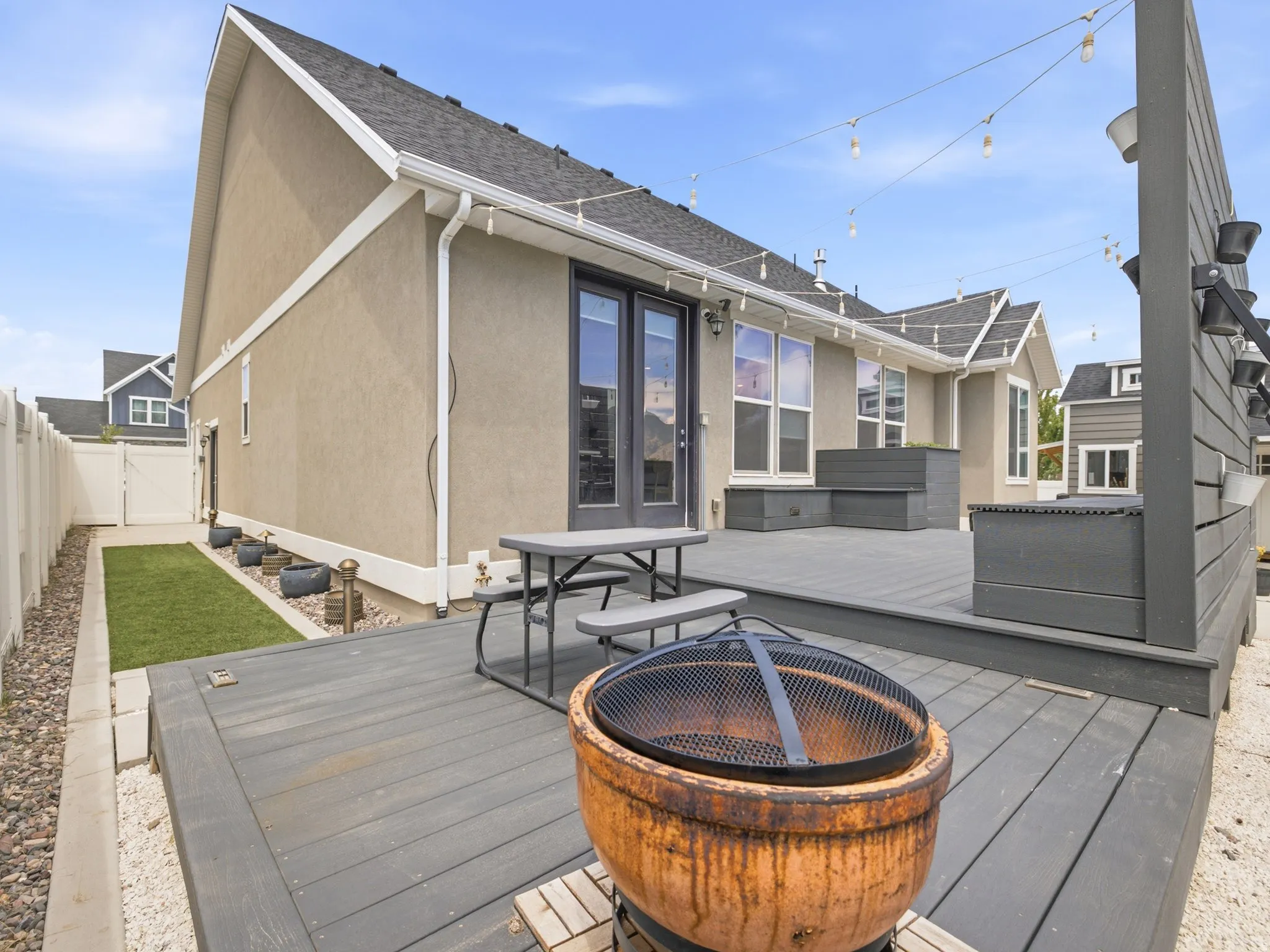 Expansive grey composite decking featuring a fire pit, string lighting, and built-in planters