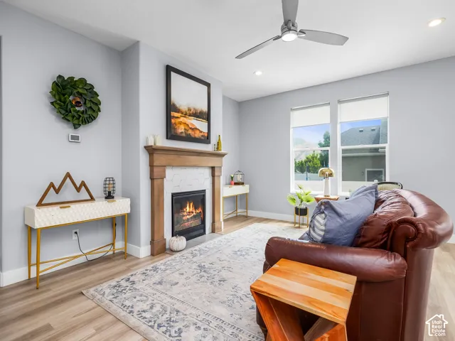 Living area featuring a gas fireplace with a wood mantle and hexagonal tile surround, light wood-finish flooring, two large windows, recessed lighting, and a ceiling fan