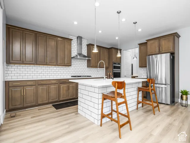 Modern kitchen featuring wood-finish cabinetry, stainless steel appliances, a subway tile backsplash, recessed lighting, and a kitchen island with pendant lighting