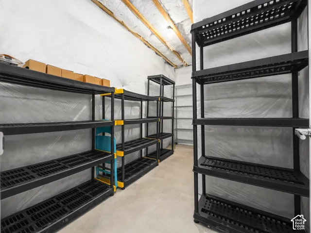 Utility room featuring exposed ceiling joists with insulation, concrete flooring, and multiple shelving units