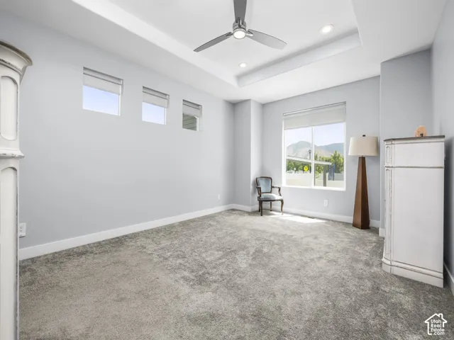Spacious interior room featuring a tray ceiling with recessed lighting and a ceiling fan