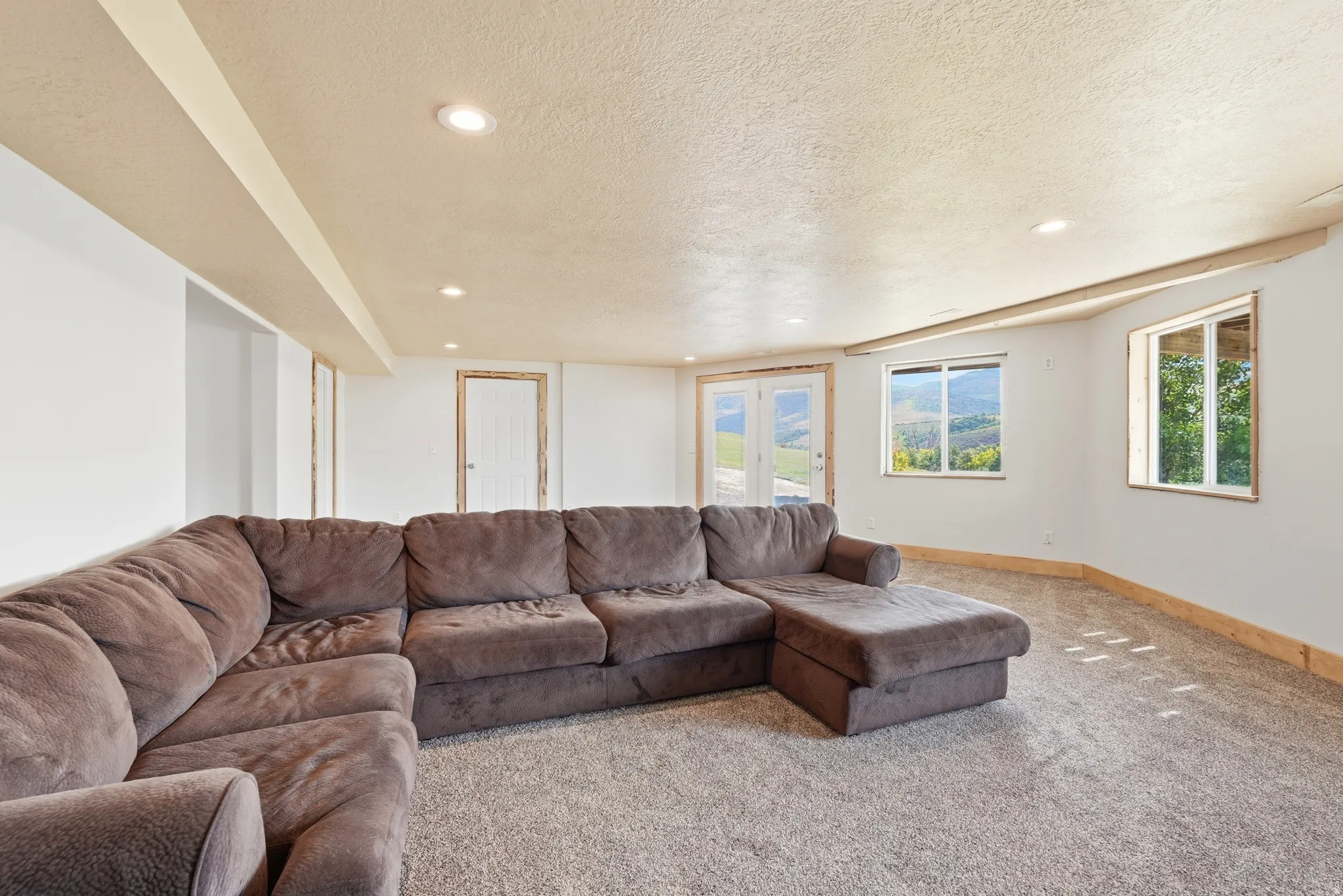 Spacious room featuring light gray carpet flooring, white walls, recessed ceiling lighting, and multiple windows offering external views