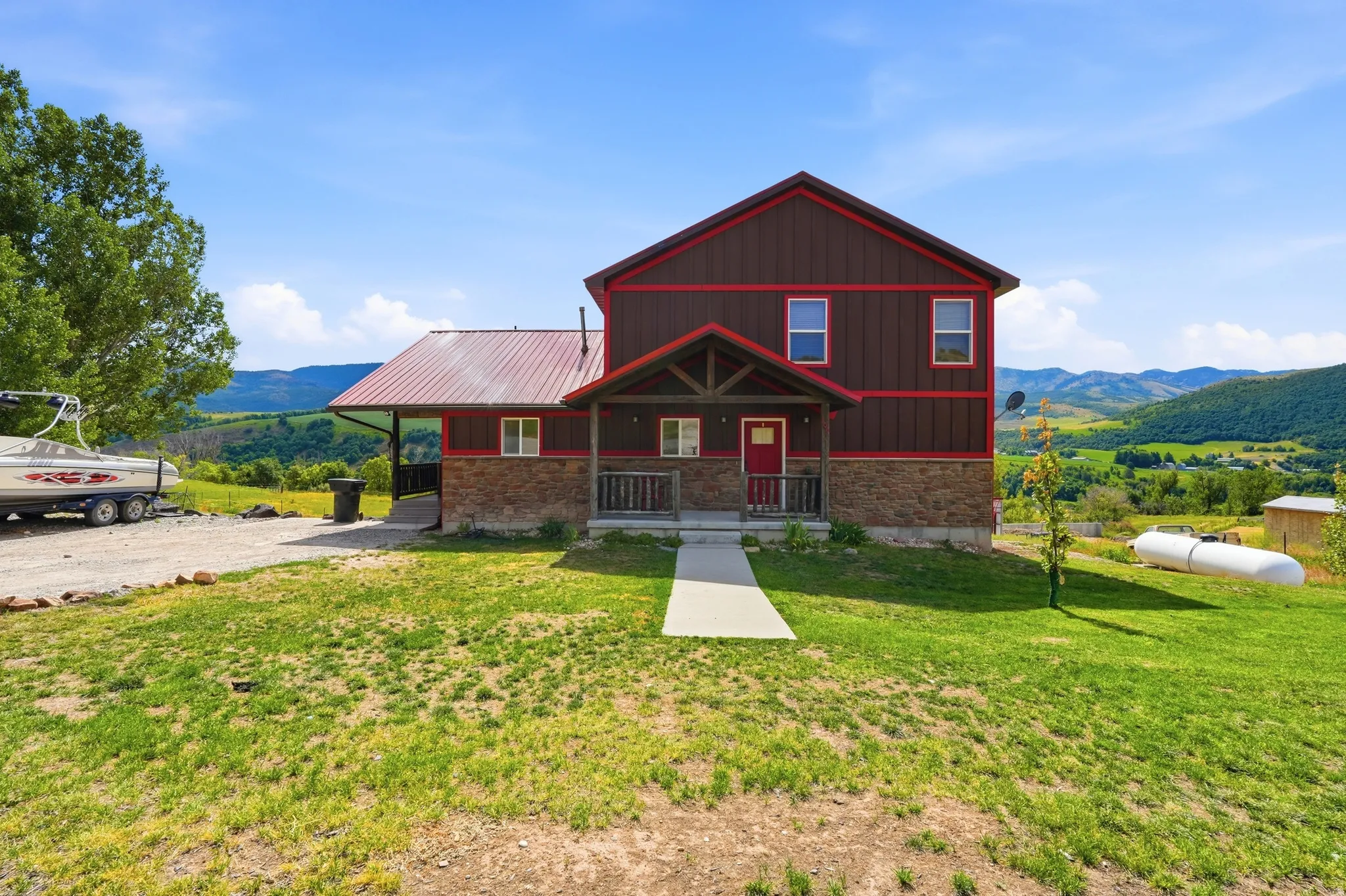 Two-story residence featuring a brown siding exterior with red trim, a red metal roof, and stone facade accents