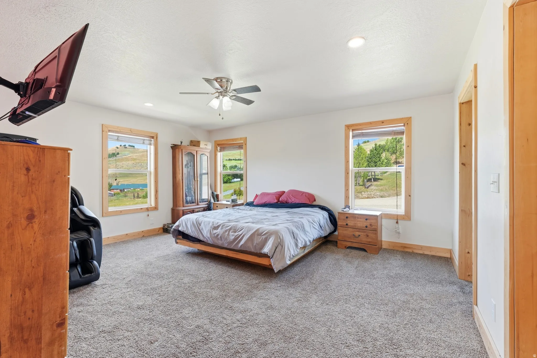 Spacious room featuring light-toned carpeting, white walls, and natural wood trim around windows and doorways
