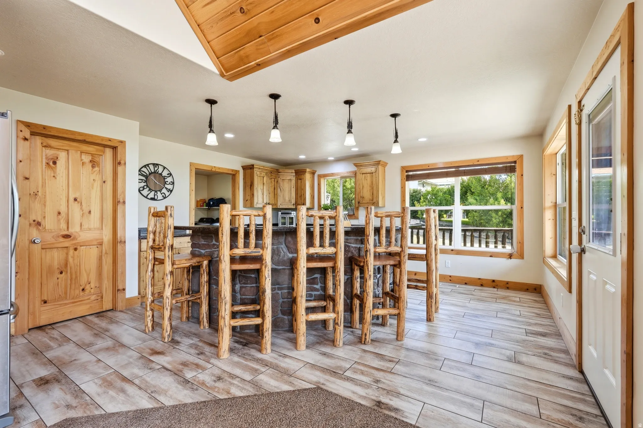 Open-concept kitchen featuring wood-finish flooring, a stone-clad island with seating, pendant lighting, wood cabinetry, and extensive natural light from multiple windows