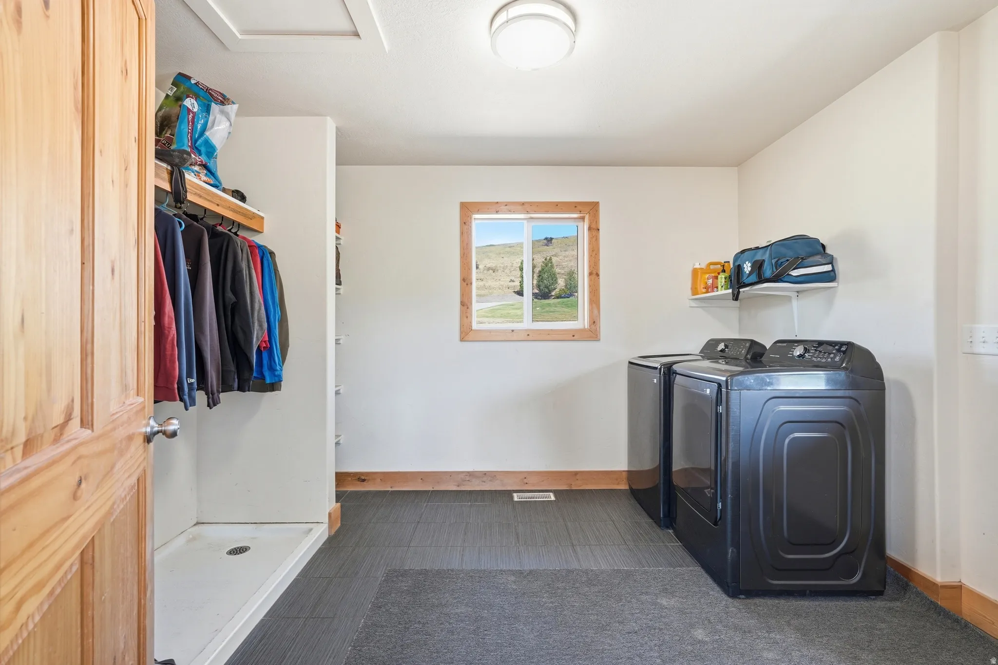 Dedicated laundry area featuring modern appliances, tile flooring, a window with wood trim, and a built-in hanging rack with shelving