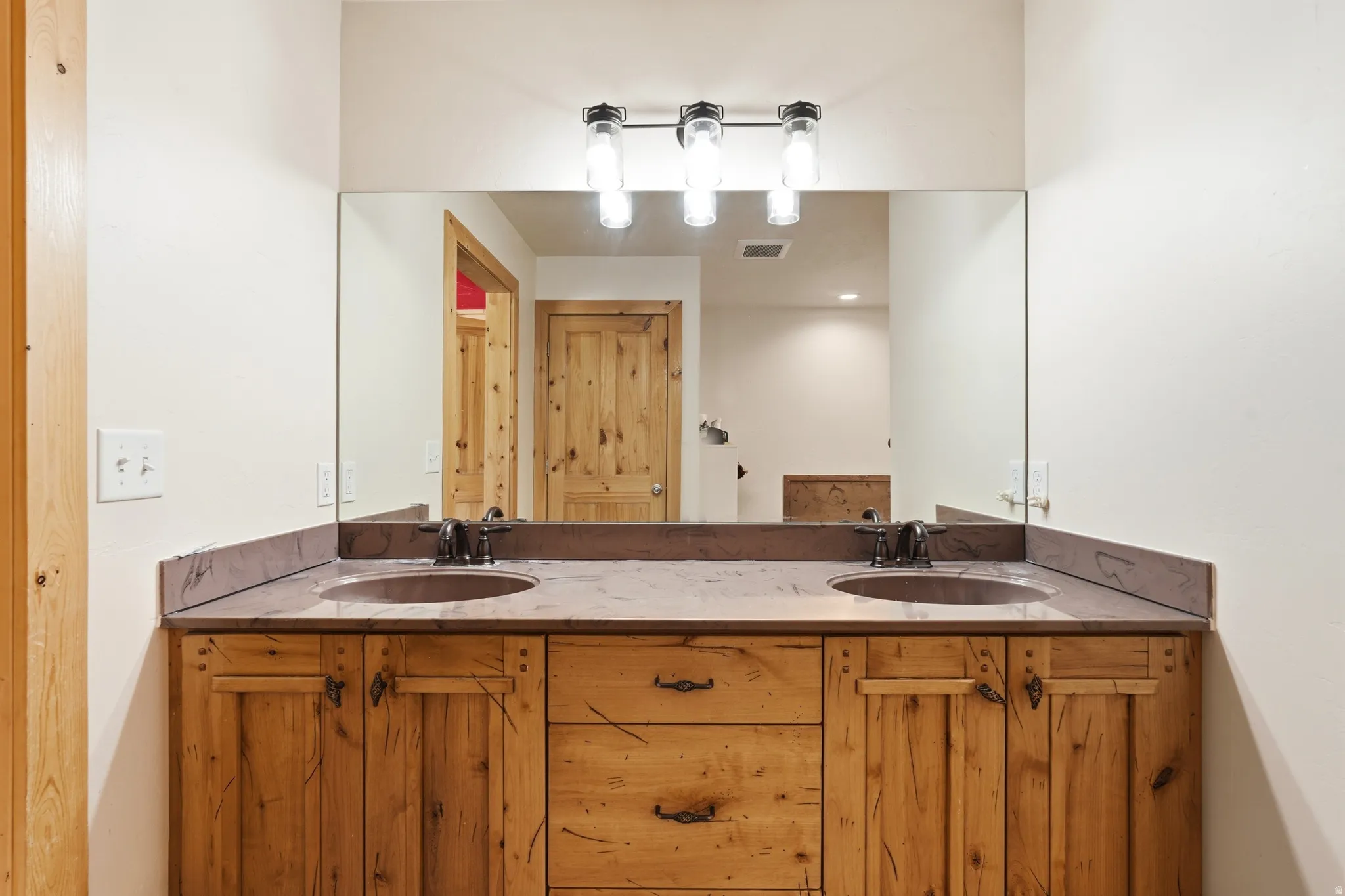 Dual basin vanity featuring wood cabinetry, stone countertops, and dark bronze fixtures