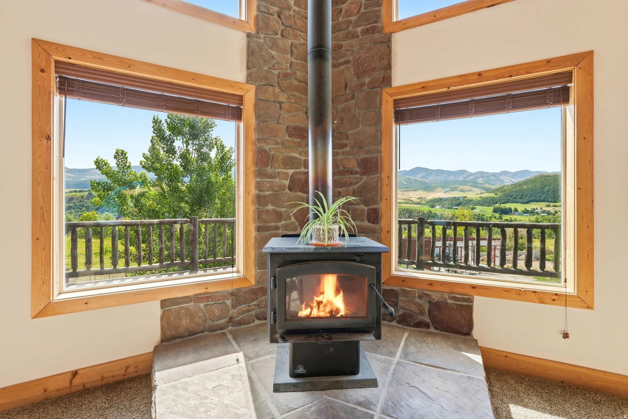 Corner wood-burning stove with a stone surround, complemented by natural wood window frames