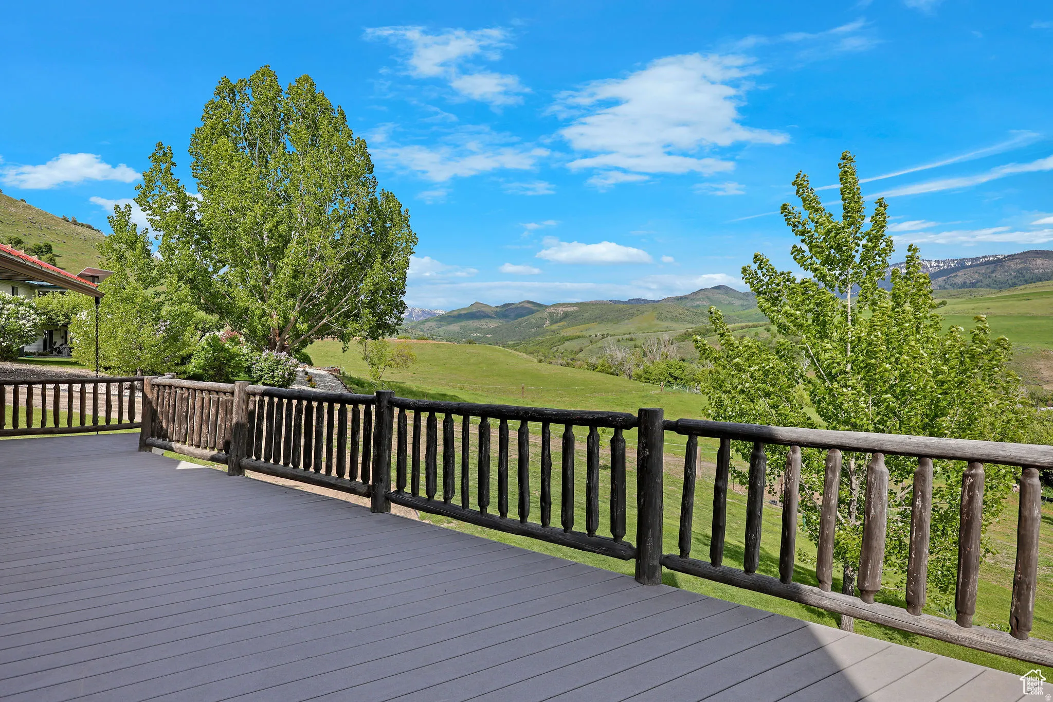 Expansive outdoor deck with gray composite decking and rustic wood railing, bordered by mature trees and verdant hills