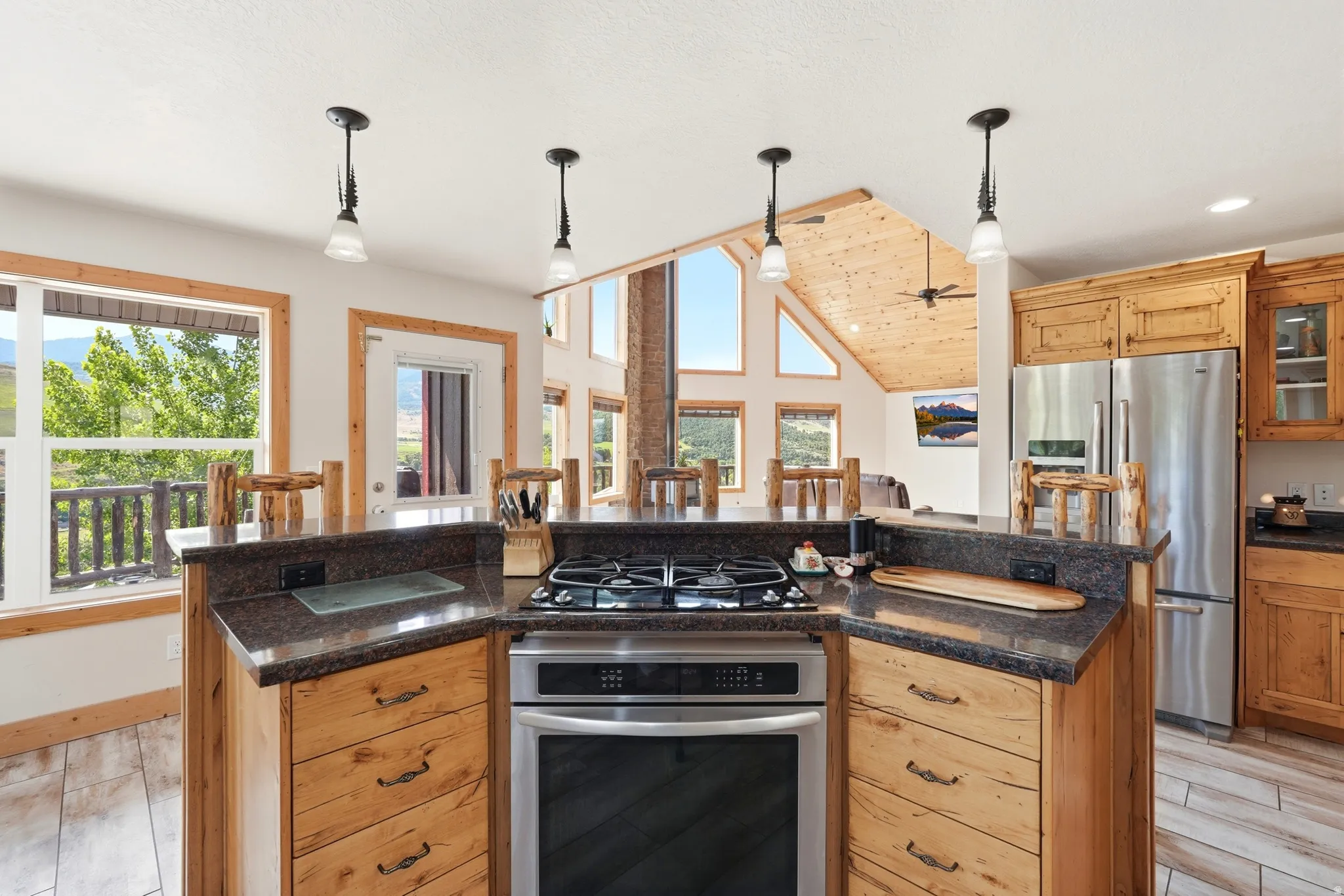 Kitchen island with built-in gas range, stainless steel appliances, wood-finish cabinetry, and dark countertops