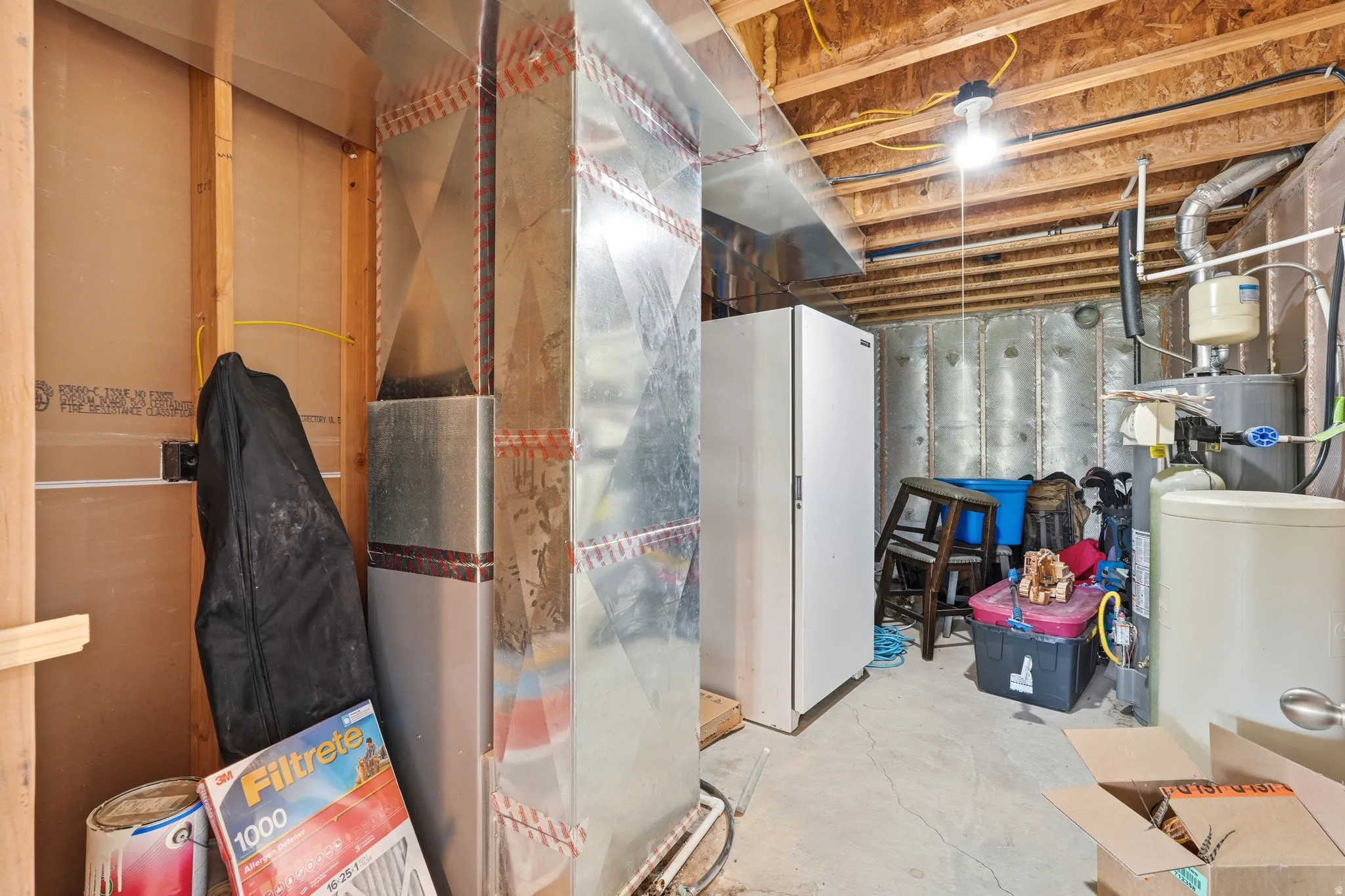 Unfinished basement area featuring exposed ceiling joists, ductwork, and utility installations including a water heater and water softener