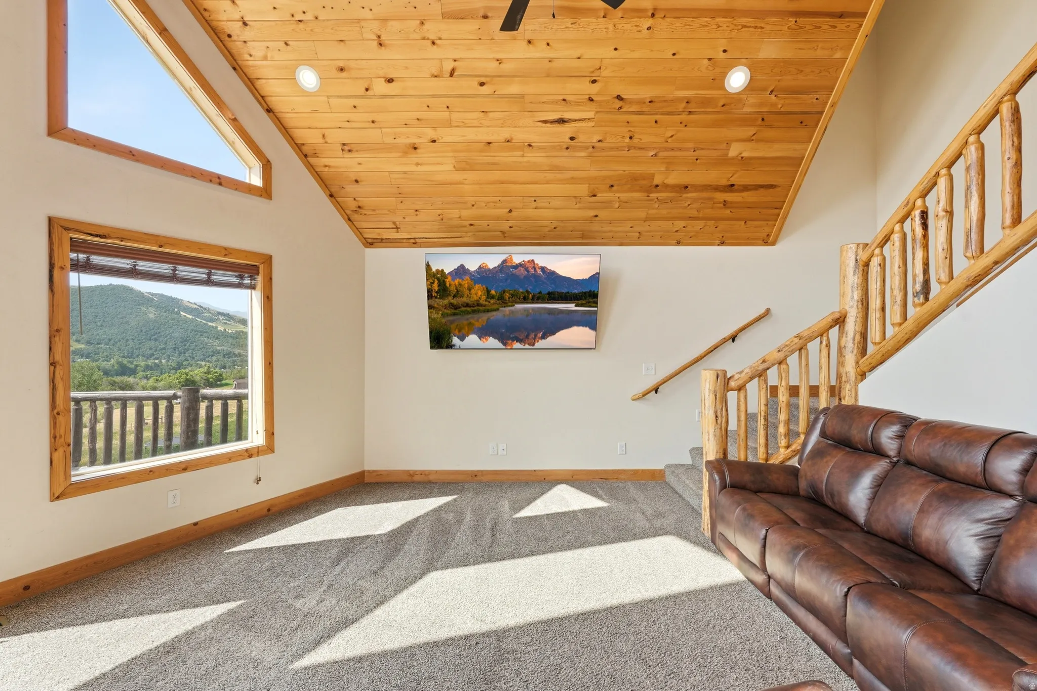 Carpeted living space featuring a wood-plank ceiling, natural wood trim windows, and a rustic log staircase