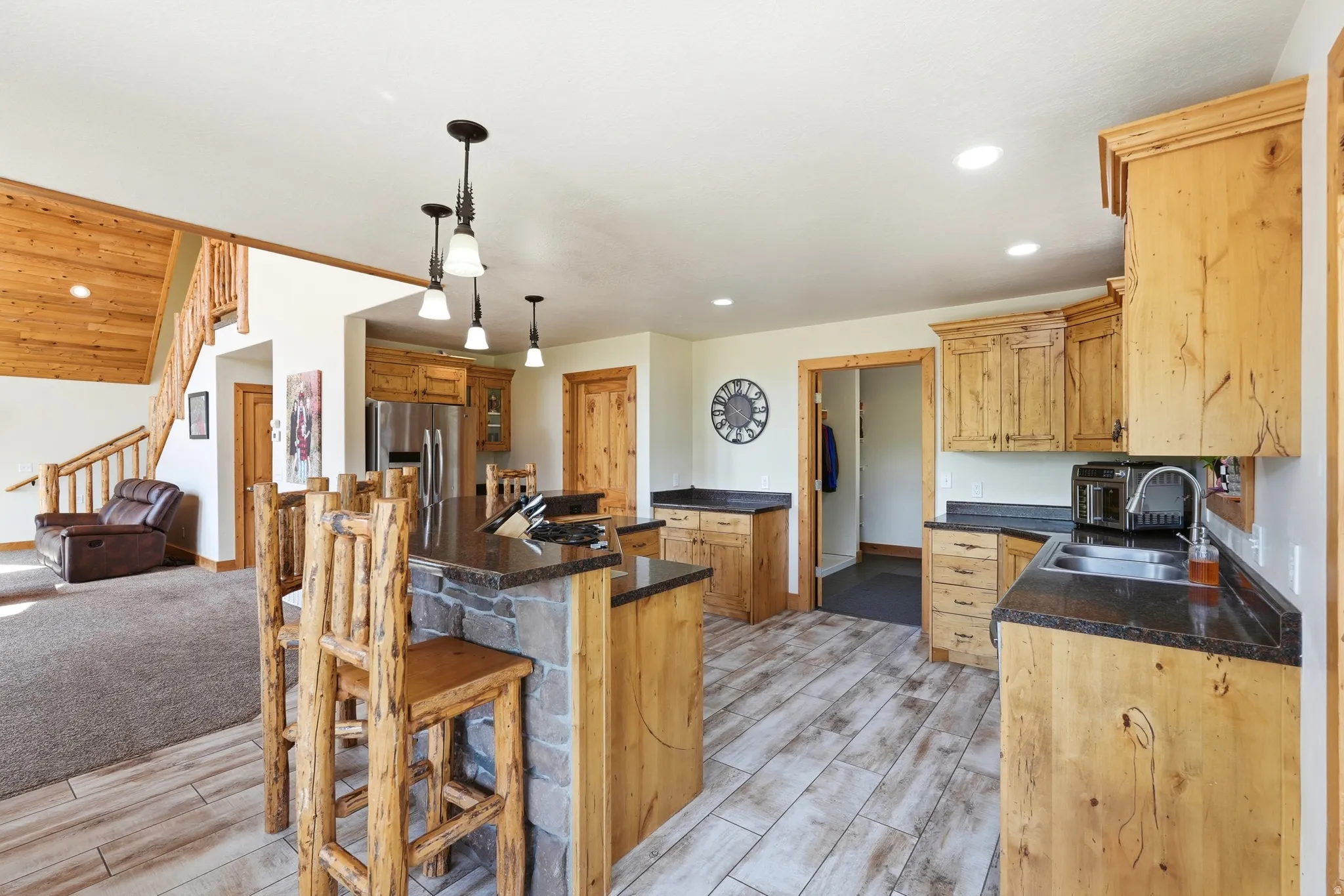 Kitchen featuring wood-finish flooring, custom wood cabinetry, dark stone countertops, and a stone-clad island with pendant lighting