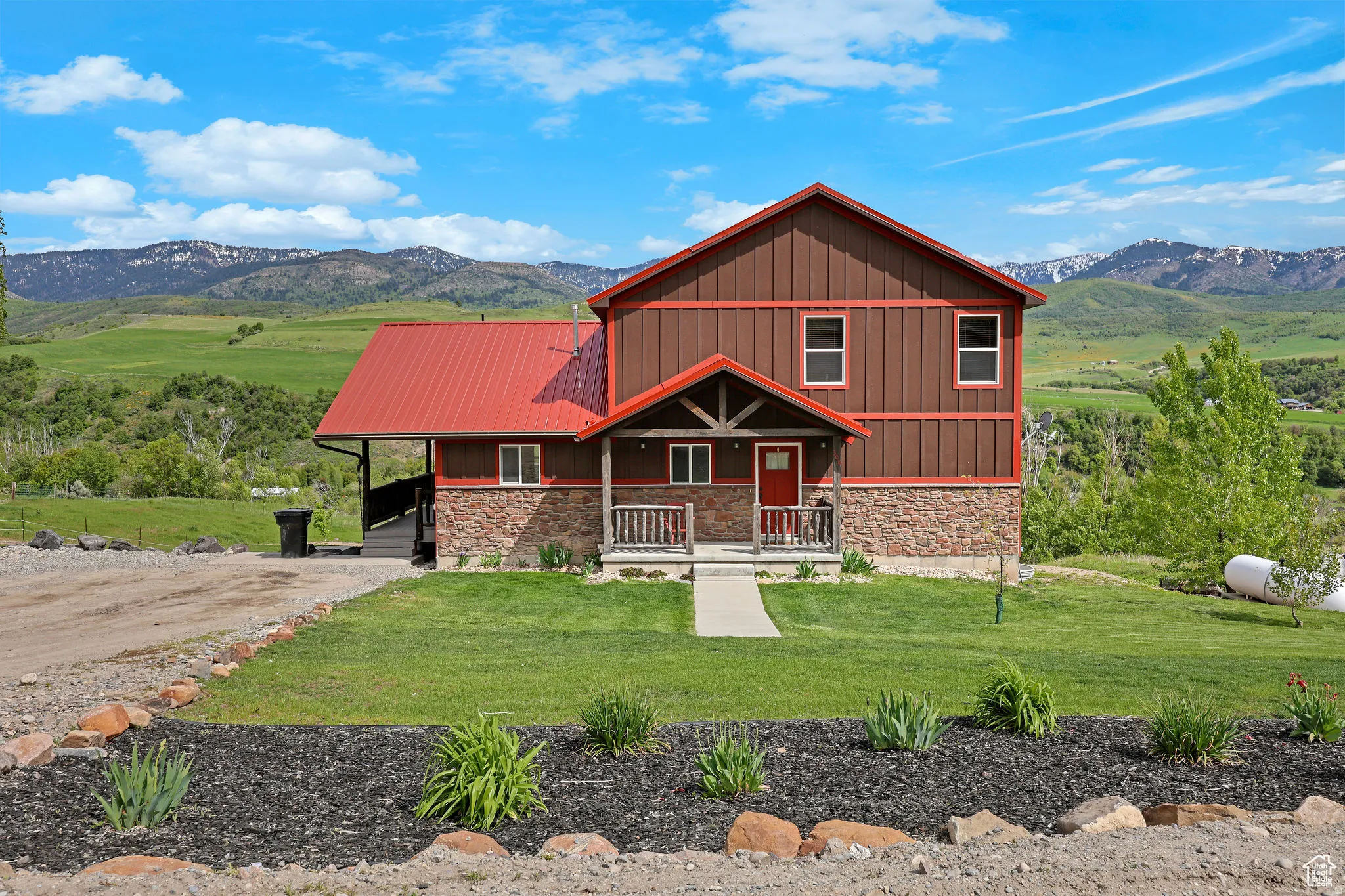 Two-story residence featuring a striking red metal roof, brown vertical siding, and a stone-clad foundation