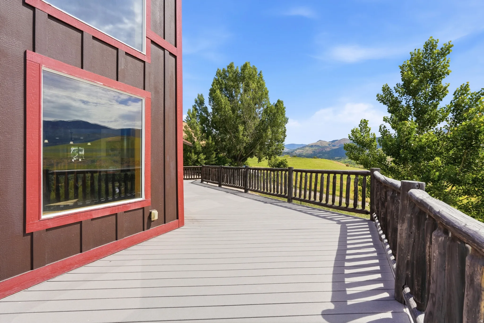 Expansive outdoor deck featuring wood-finish flooring, a rustic wood railing, and a brown vertical siding exterior with red trim