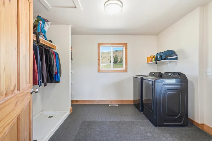 Dedicated laundry area featuring modern appliances, tile flooring, a window with wood trim, and a built-in hanging rack with shelving