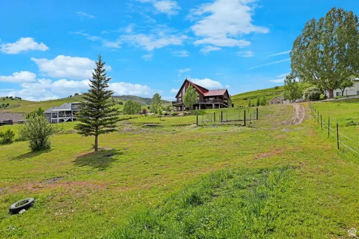 Expansive sloping green landscape with a dirt path leading towards a red-roofed residence featuring a raised deck