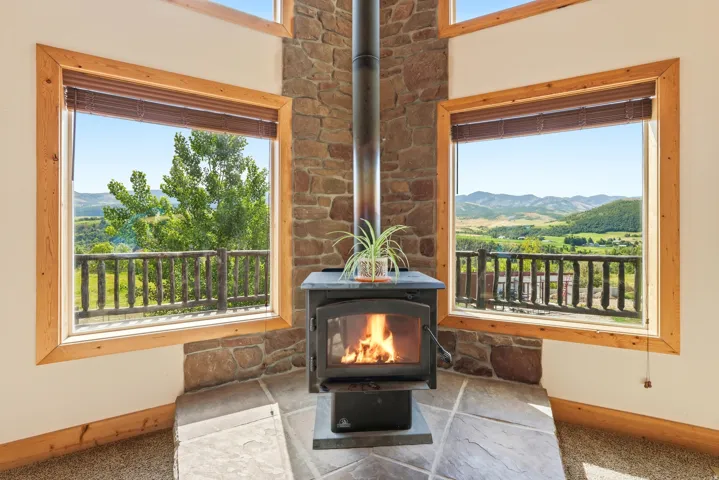 Corner wood-burning stove with a stone surround, complemented by natural wood window frames