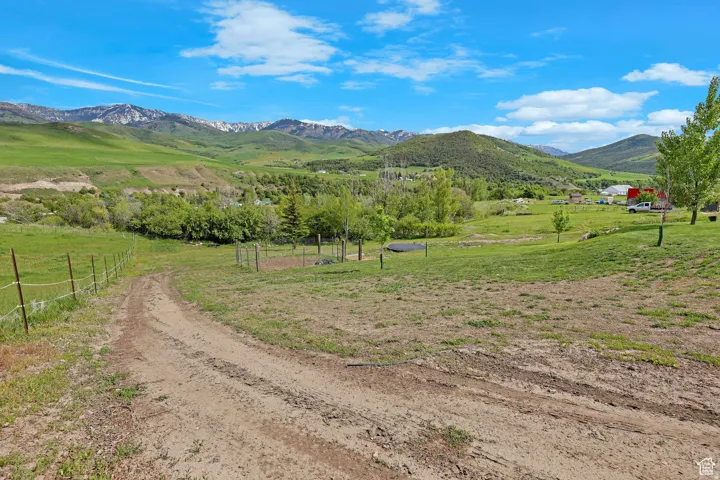 Expansive rural property featuring an unpaved access road, partial fencing, varied topography, mature trees, and distant snow-capped mountains