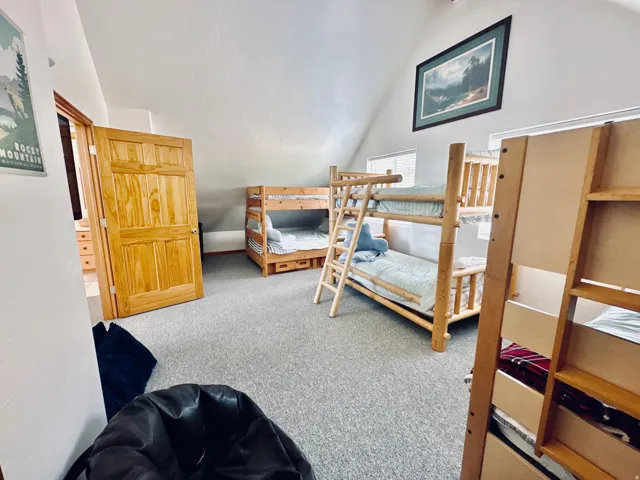 Carpeted loft area featuring a vaulted ceiling, natural wood bunk beds, and multiple windows allowing natural light