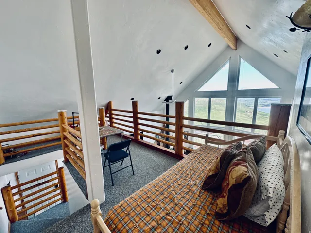 Loft area featuring vaulted ceilings with exposed wood beams, recessed lighting, and a prominent triangular window arrangement
