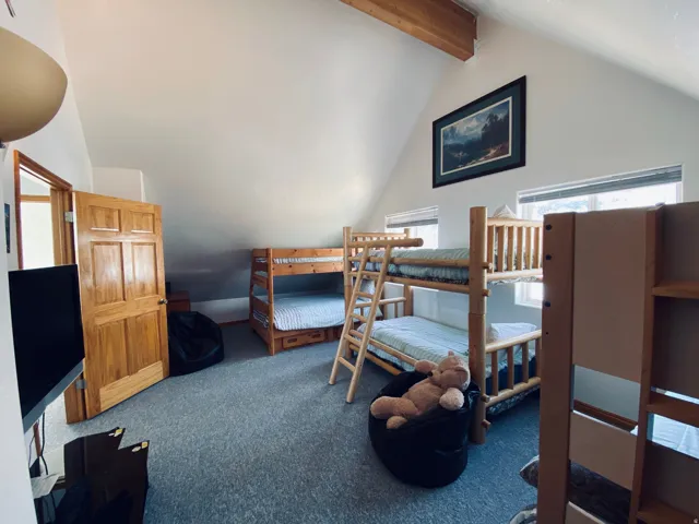 Sloped ceilings with exposed wood beams, gray carpeting, and natural wood doors