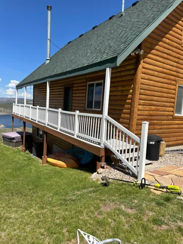 Log cabin exterior featuring a covered deck with white railings, a green shingle roof, and a stone walkway