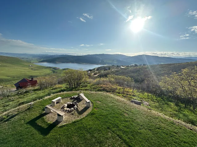 Hillside property featuring a built-in fire pit with stone surround and four stone benches, a manicured lawn, and distant lake and mountain scenery